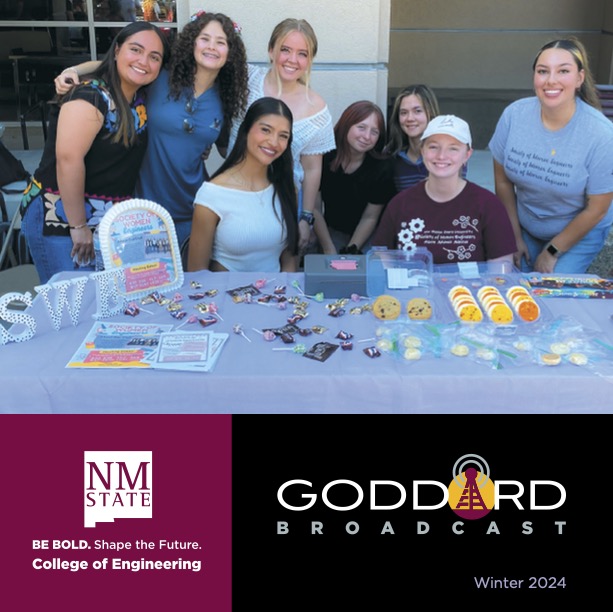 Group of students and staff posing behind a table of giveaways at a campus event, with NM State College of Engineering and Goddard Broadcast branding and “Winter 2024” text below.