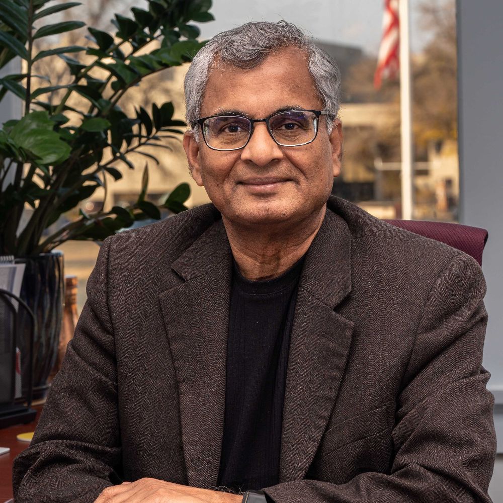 Older gentleman in an office, wearing glasses, and a dark brown suit 