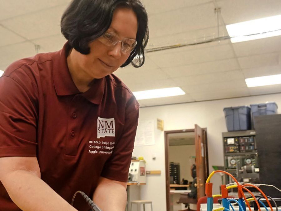 Woman in a maroon shirt, that is wearing safety glasses in a lab.